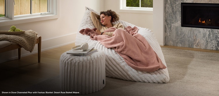 Woman sitting on a Lovesac PillowSac Accent Chair with lightweight Footsac Blanket